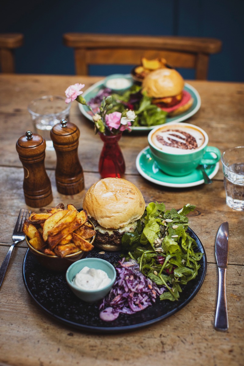 A burger with chips, salad and a flat white on a scrubbed wooden table at The Warren