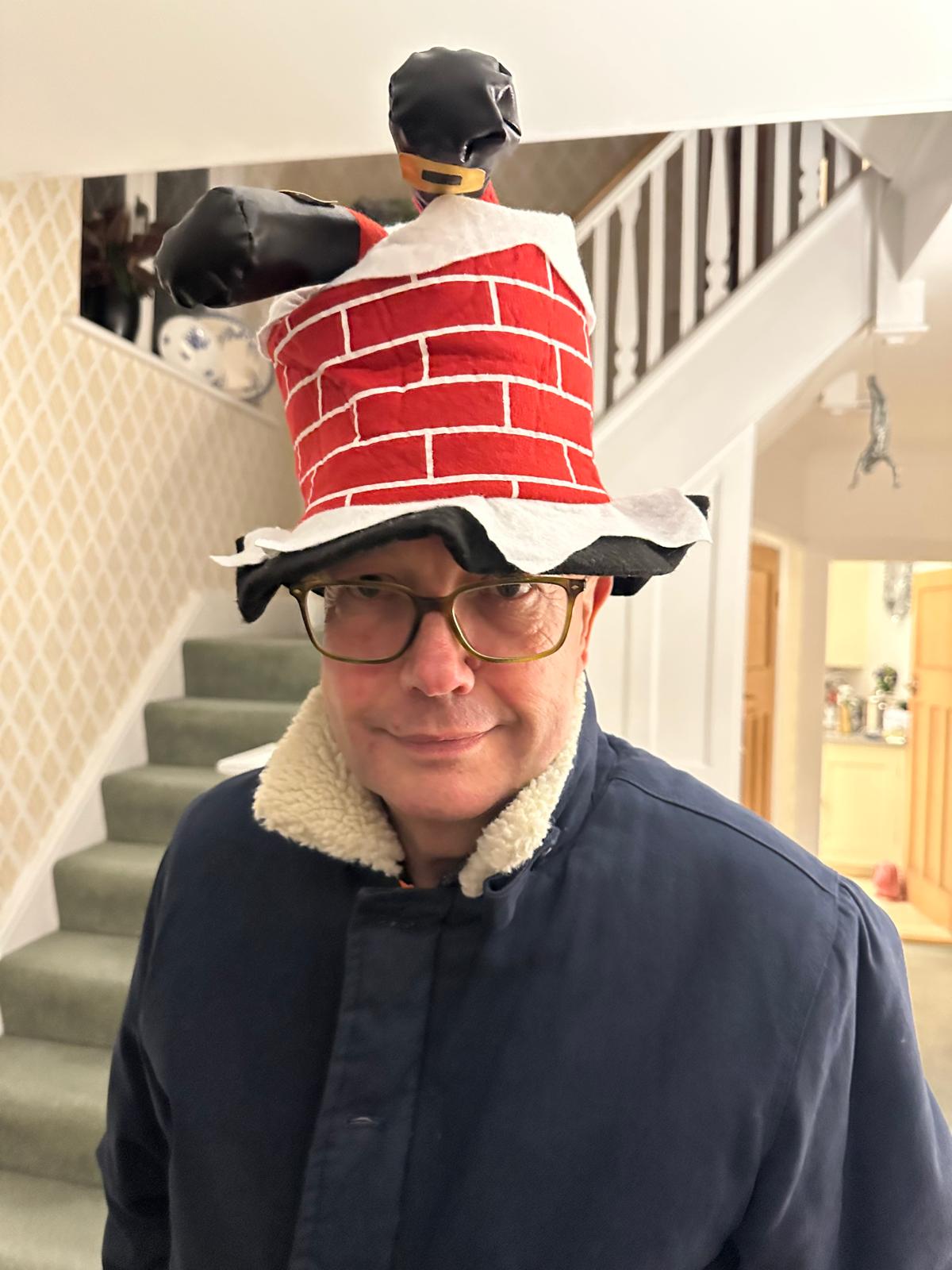 John in a chimney-pot hat by the stairs, smiling