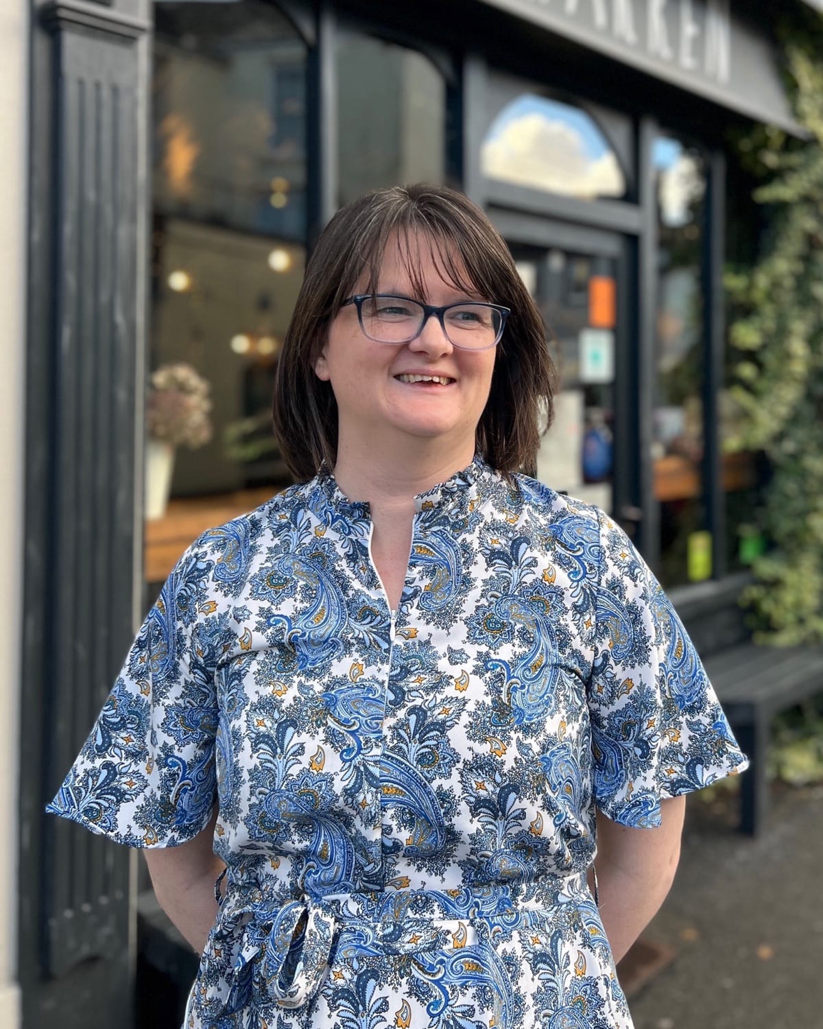 Meleri smiling outside the front of The Warren, in a blue paisley dress