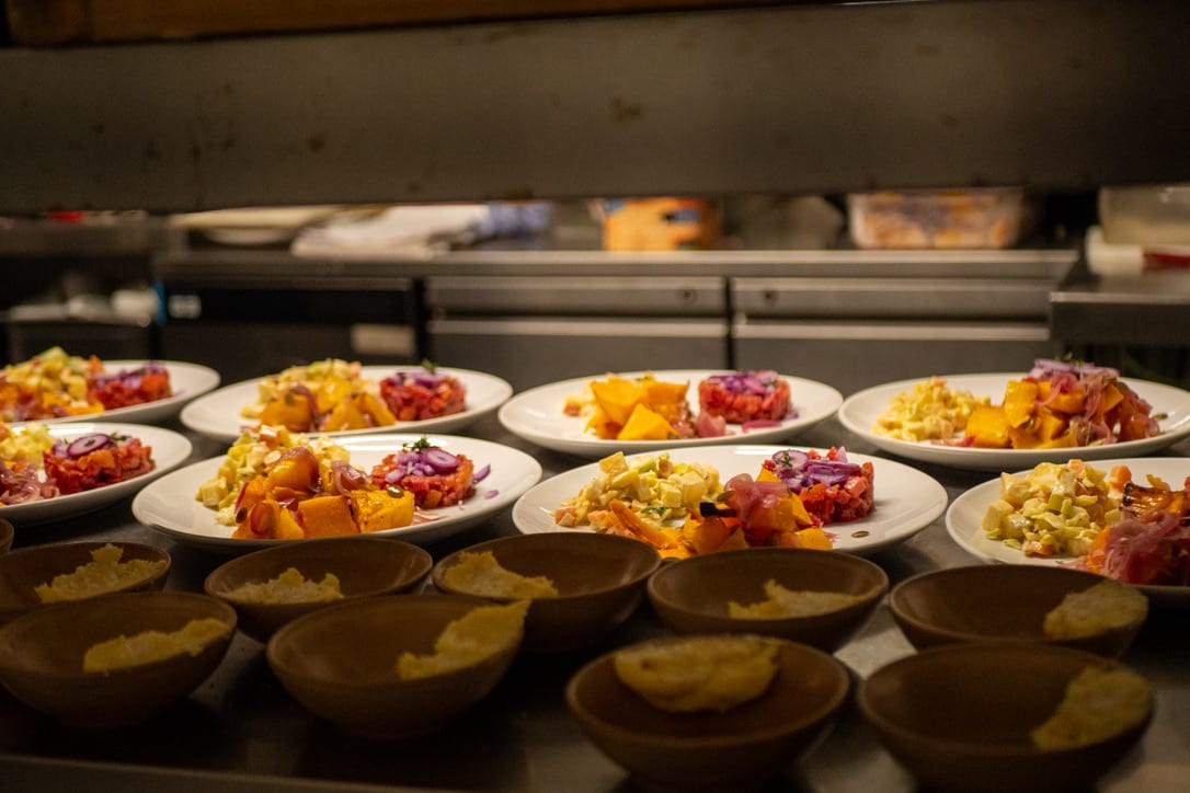 Plated starters lined up along the pass at The Warren, ready to go out, with bread bowls in front of them