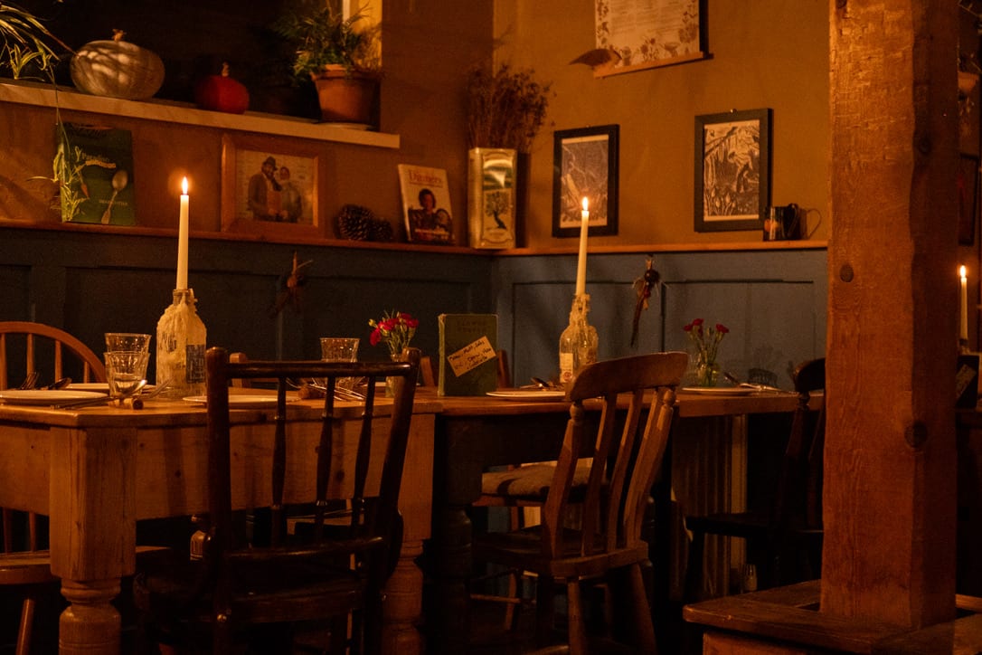 Tables laid for lunch at The Warren, candles lit, wooden chairs and flowers on the tables