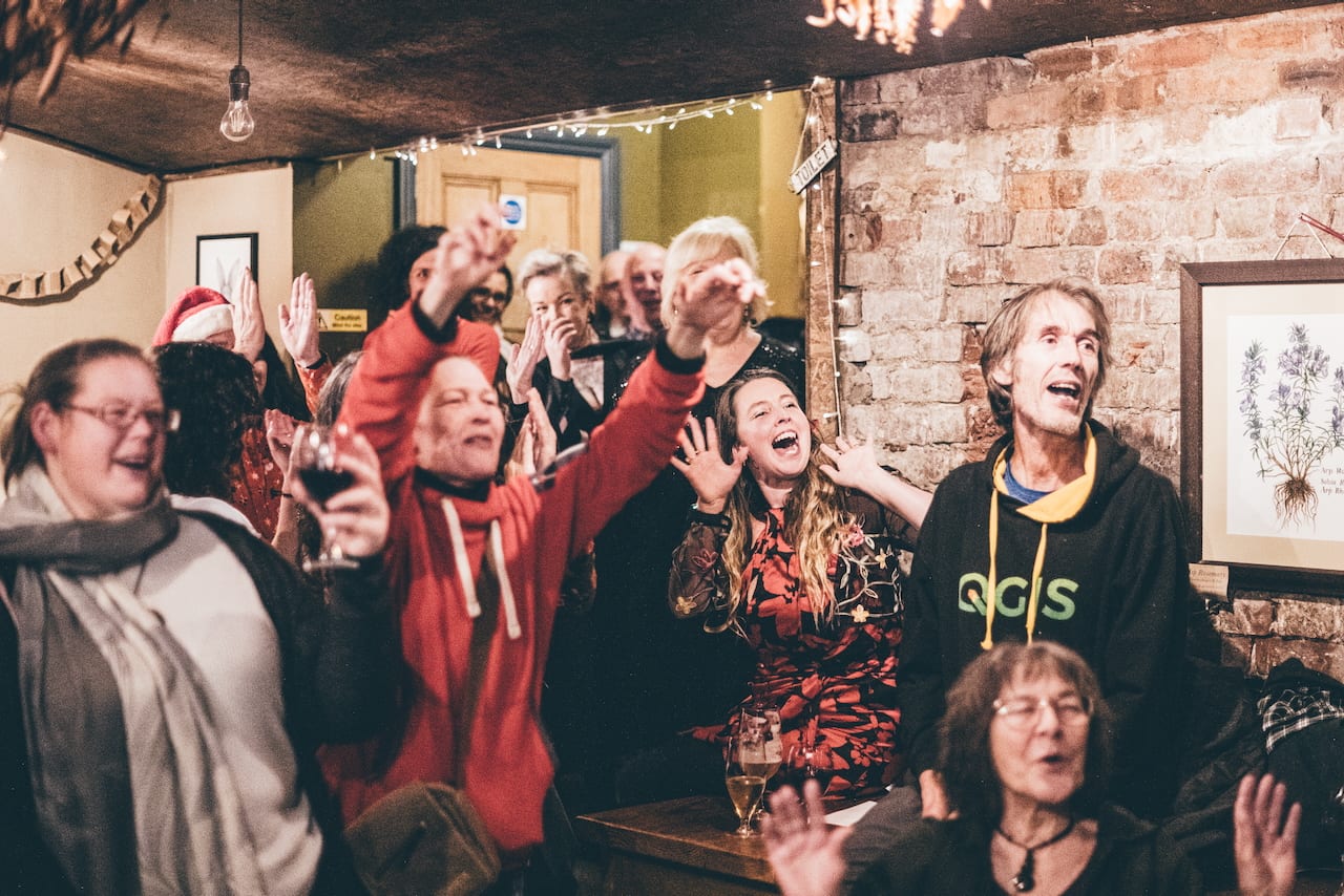 A room full of people at The Warren, arms in the air, mid cheer