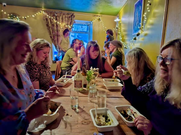 A long table of friends sharing food and wine under fairy lights
