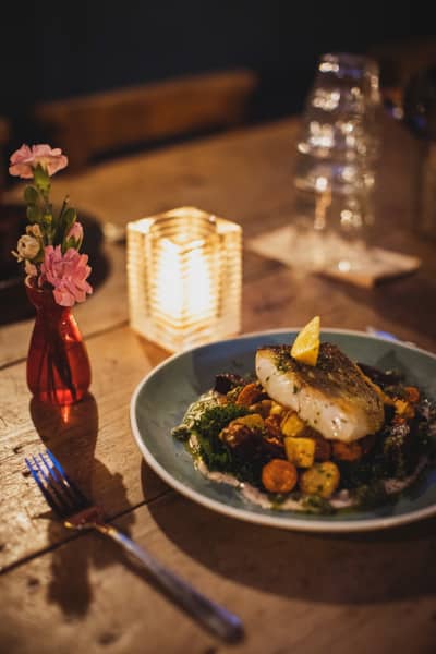 Fish on greens, beside a candle and a vase of flowers