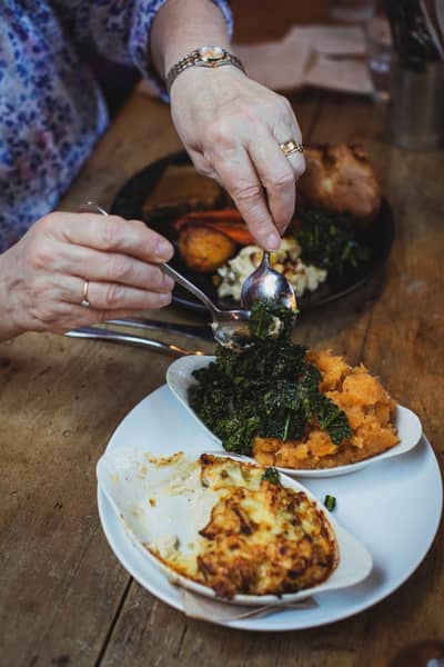 Sharing dishes of greens and gratin passed across the table